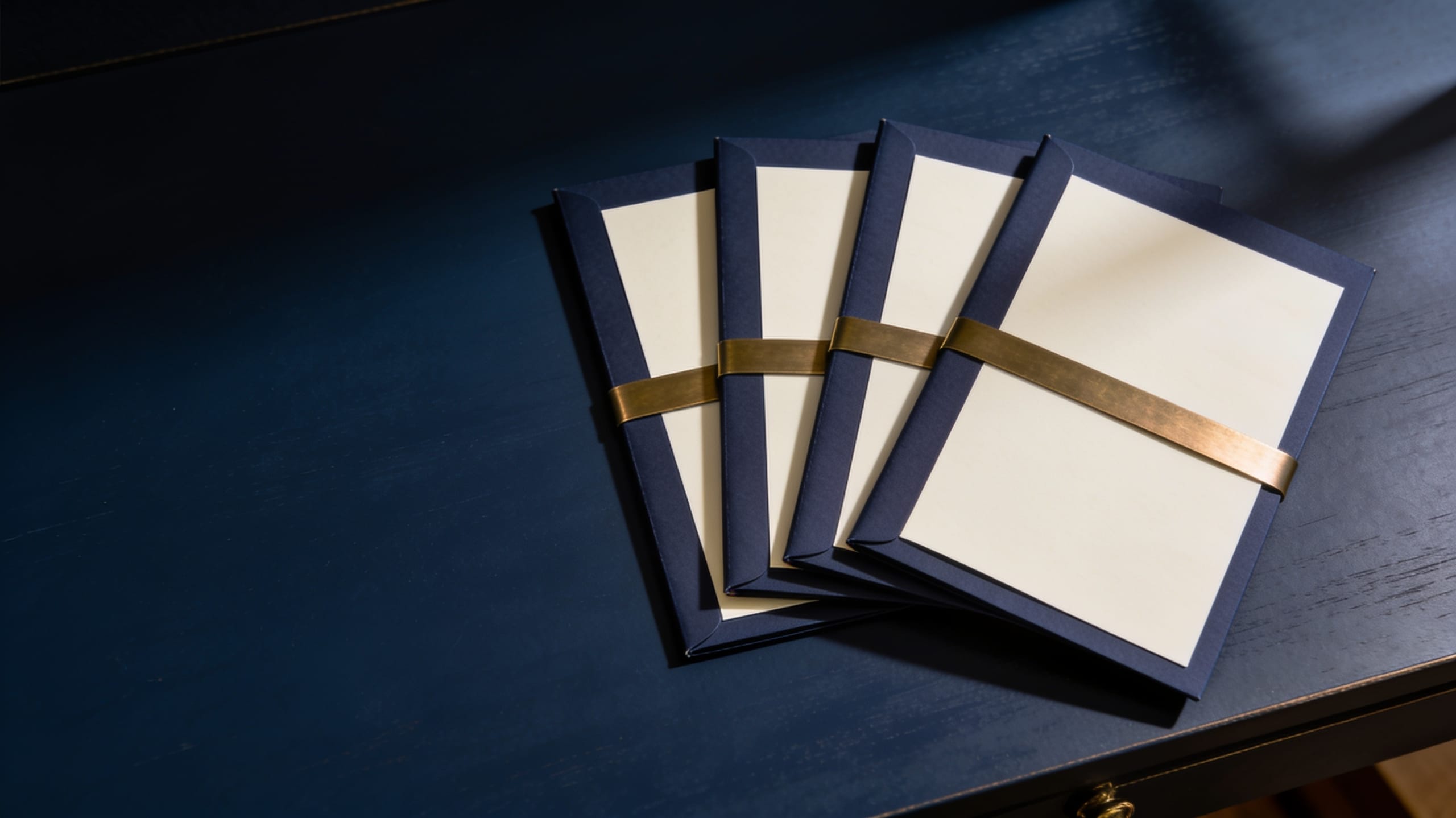 Four navy folders of blank paper held together by one brass band
